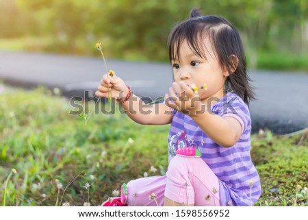 Portrait​ image​ of​ 1​-2​ years​ old​ baby.​ Happy​ Asian child girl picking and touching the flowers and​ grass​ at the garden field. Learning, exploring​ and​ development​ of​ kid​ concept.