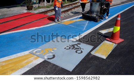 Road workers group with thermoplastic spray road marking machine are working to paint traffic sign and bicycle lane on asphalt road with railway track crossing on street surface