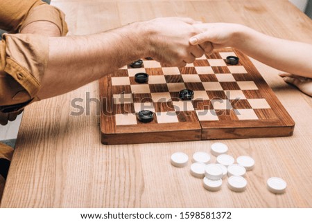 Cropped view of man and woman handshaking by checkerboard at table