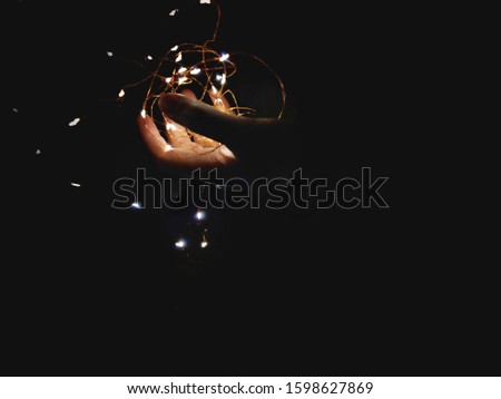 person holding fairy lights in hand with black background