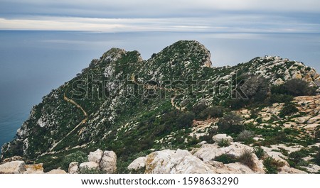 Huge cliff covered with vegetation and Mediterranean Sea cloudy sky photo taken on top of Penon de ifach Natural Park, no people. Beautiful landscape background. Calpe, Alicante, Costa Blanca, Spain
