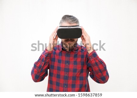 Handsome middle aged aged man in VR headset. Focused man in checkered shirt using virtual reality headset on grey background. Technology concept