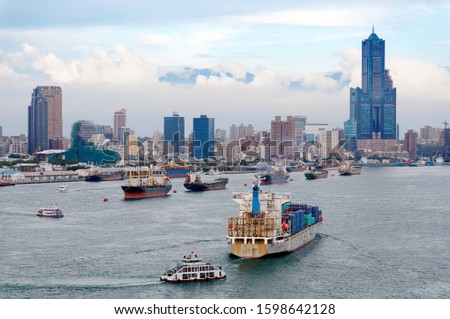 A cargo ship makes its way into Kaohsiung Harbor with the landmark 85 Sky Tower standing out among high-rise buildings and various vessels parking & navigating in the seaport on a cloudy summer day Royalty-Free Stock Photo #1598642128