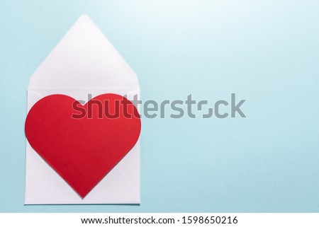 St. Valentine’s Day greeting card with big red heart and white envelope on blue pastel background.