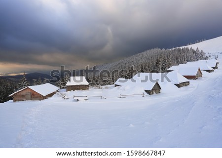 Majestic winter scenery. Dramatic sky. Old wooden huts on the lawn covered with snow. Landscape of high mountains and forests. Wallpaper background. Location place Carpathian, Ukraine, Europe.