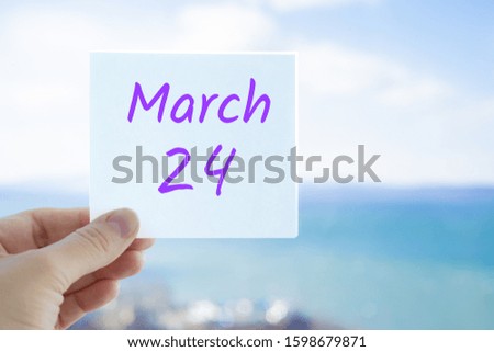 March 24th. Hand holding sticker with text March 24 on the blurred background of the sea and sky. Copy space for text. Spring month in calendar concept