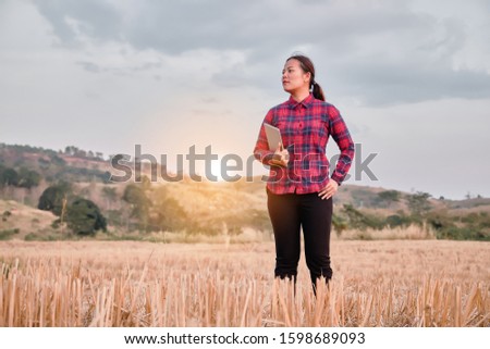 Asian Female farmer standing in a field and holding tablet and examining.