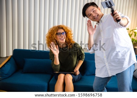 Asian guy using smartphone while making video with pretty lady in the office stock photo