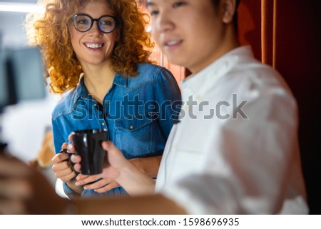 Smiling young woman holding cup of hot drink near male employee stock photo
