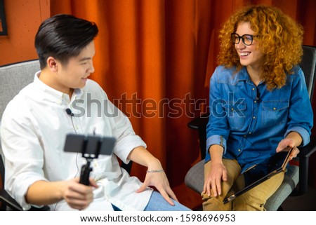 Waist up of smiling two colleagues talking while recording an interview stock photo
