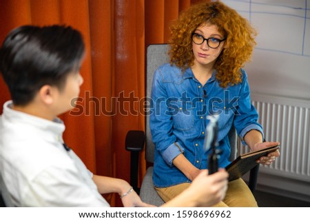 Young guy holding smartphone while making video with his female colleague stock photo
