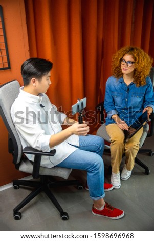 Two colleagues sitting in office chairs with gadgets while recording video stock photo