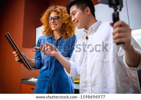 Happy Asian man holding smartphone while looking at tablet screen stock photo