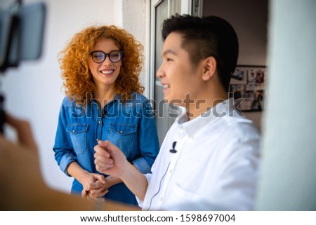 Smiling Asian guy asking questions for pretty lady while making video stock photo