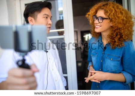 Male blogger using phone while recording an interview with smiling lady stock photo