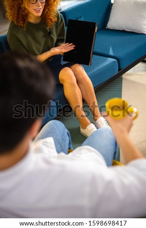 Young lady in glasses on sofa using gadget while recording interview with guy stock photo