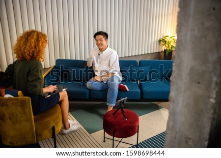 Happy Asian man sitting on sofa while recording vlog in office stock photo