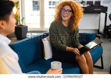 Female showing touchpad to Asian guy while they are making vlog in office stock photo