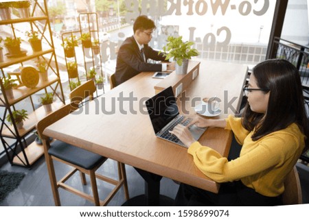 A young business man in a black suit and beautiful  woman wear a yellow sweater and sit in different corners of the coffee shop.