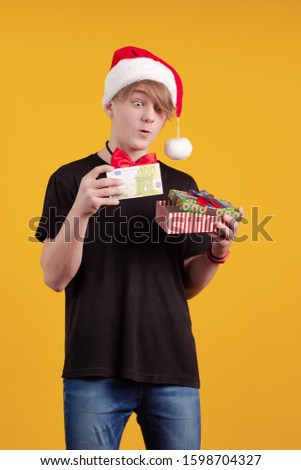 A young guy in a red Santa Claus hat holds in his hands banknotes, money and posing on a yellow background