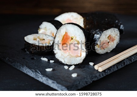 rolls with rice fish and tomato on a stone board, japanese food on a dark wooden background and chopsticks