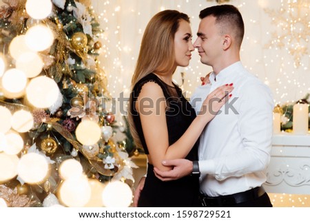 An attractive couple in love embrace and enjoy Christmas holiday together. Couple in love kisses and hugs near the Christmas tree lights. New year's night.Christmas.