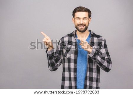 Look over there! Happy young handsome man in casual pointing away and smiling while standing against gray grey white background.