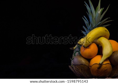 Bowl with fruit. pineapple, banana, kiwi, orange, tangerine against black background