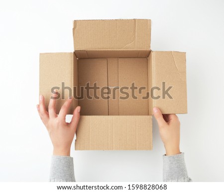 open empty square brown cardboard box for transportation and packaging of goods and two hands take out items, view from the top