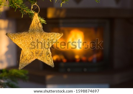 Photo of burning fireplace next to decorated Christmas tree with golden star