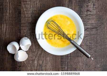 Raw eggs in white bowl with metal whisk, three eggshells, wood table
 Royalty-Free Stock Photo #1598889868