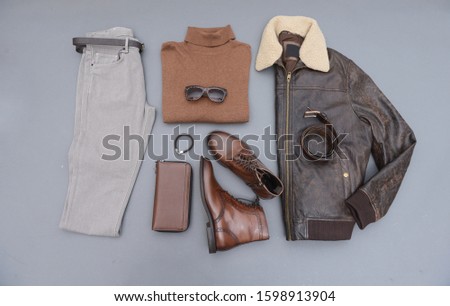 Fashion leather jacket with khaki pants and brown boots shoes,sunglasses, purse, sweater isolated on gray background
