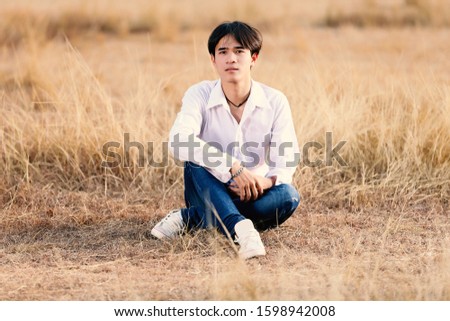 
A teenager wearing a white shirt, jeans ordered to take pictures in the meadow Tell about resolute