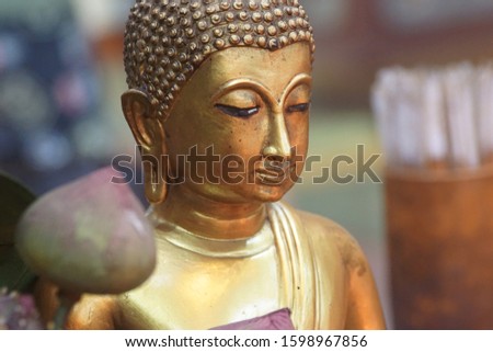 Selective focus on a face of old Buddha statue with blurred of a lotus flower on the front and cylinder of bamboo on background at Chinese temple in Thailand. Wealthy and abound concept.