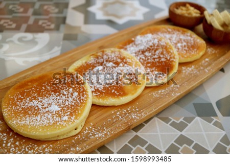 Pancakes with icing sugar on wooden plate served on patterned stone table