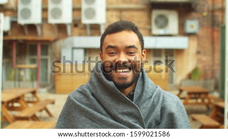 Man in grey blanket stand on the street, smile and laugh