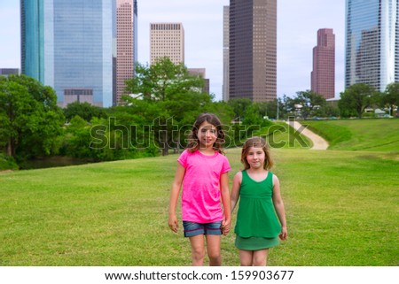 Two sister girls friends walking holding hand in urban modern skyline on grass lawn
