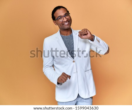 Portrait of a young African American man with short haircuts and a white-toothed smile in a white jacket on a pink background. Standing and talking right in front of the camera.
