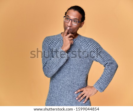Portrait of a young African American man in glasses with a short haircut and with a white-toothed smile in a gray sweater on a pink background. Standing and talking right in front of the camera.