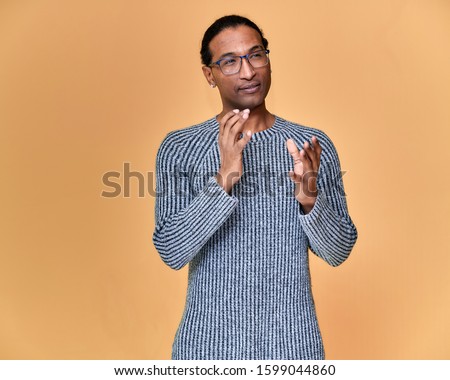 Portrait of a young African American man in glasses with a short haircut and with a white-toothed smile in a gray sweater on a pink background. Standing and talking right in front of the camera.
