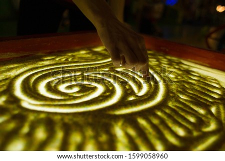 Drawings in the sand. Art therapy. Sand animation. Female fingers draw a heart in the sand. The development of the imagination. Patterns. Backlit table.