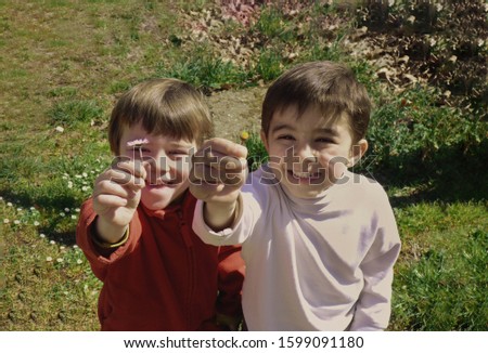 Adorable twins smiling and offering a flower, happy children playing in the field