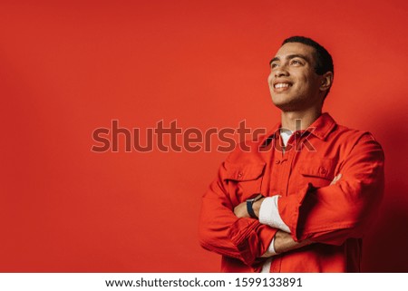 Side view of positive arabian egyptian guy posing and smiling. Stand with hands crossed. Happy positive man isolated over red background