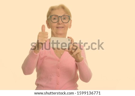 Happy senior nerd woman smiling while taking picture with mobile phone and giving thumb up