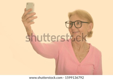Happy senior nerd woman smiling and taking selfie with mobile phone