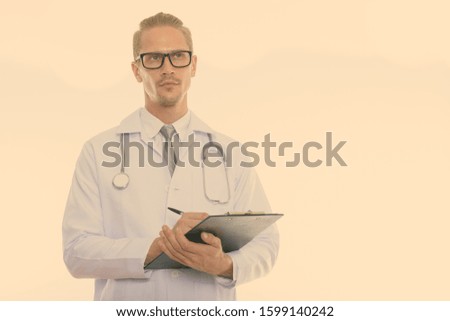 Studio shot of young handsome man doctor writing on clipboard while thinking and looking up