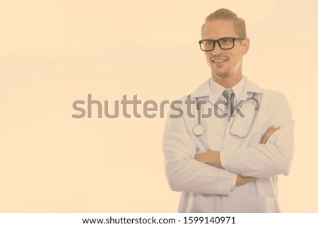 Studio shot of happy handsome man doctor smiling and thinking with arms crossed