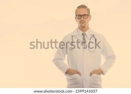 Studio shot of young handsome man doctor with hands on pockets