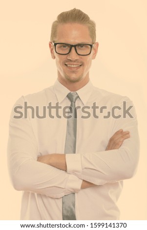 Studio shot of young happy businessman smiling and wearing eyeglasses with arms crossed