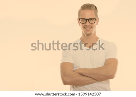 Studio shot of young happy man smiling while wearing eyeglasses with arms crossed